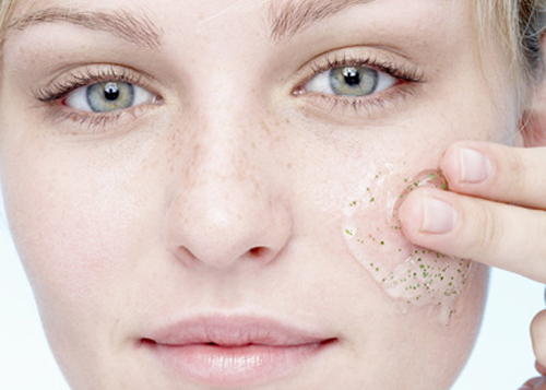 Young woman applying exfoliating gel to face, portrait, close-up