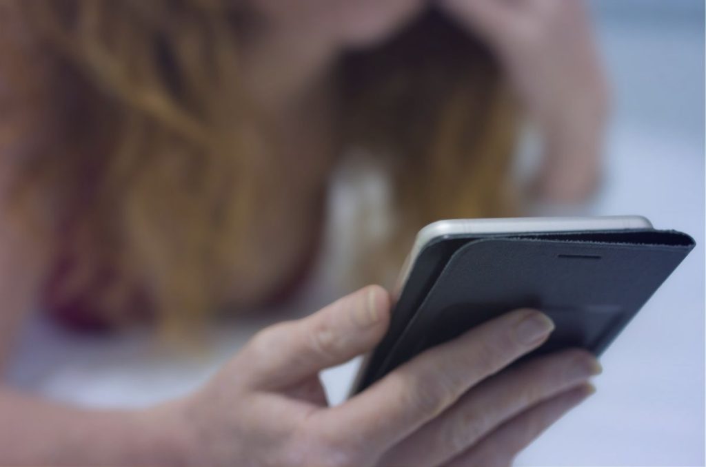 Mujer sosteniendo su celular, enfocada en la pantalla, sin mostrar su rostro.