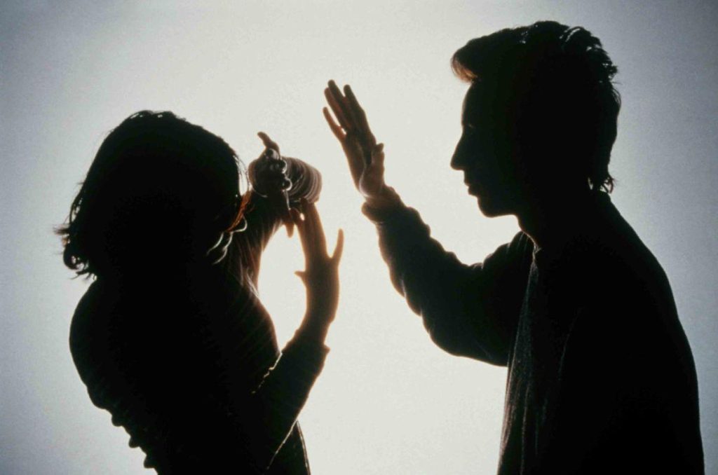 Siluetas de un hombre levantando la mano de forma amenazante frente a una mujer que intenta protegerse