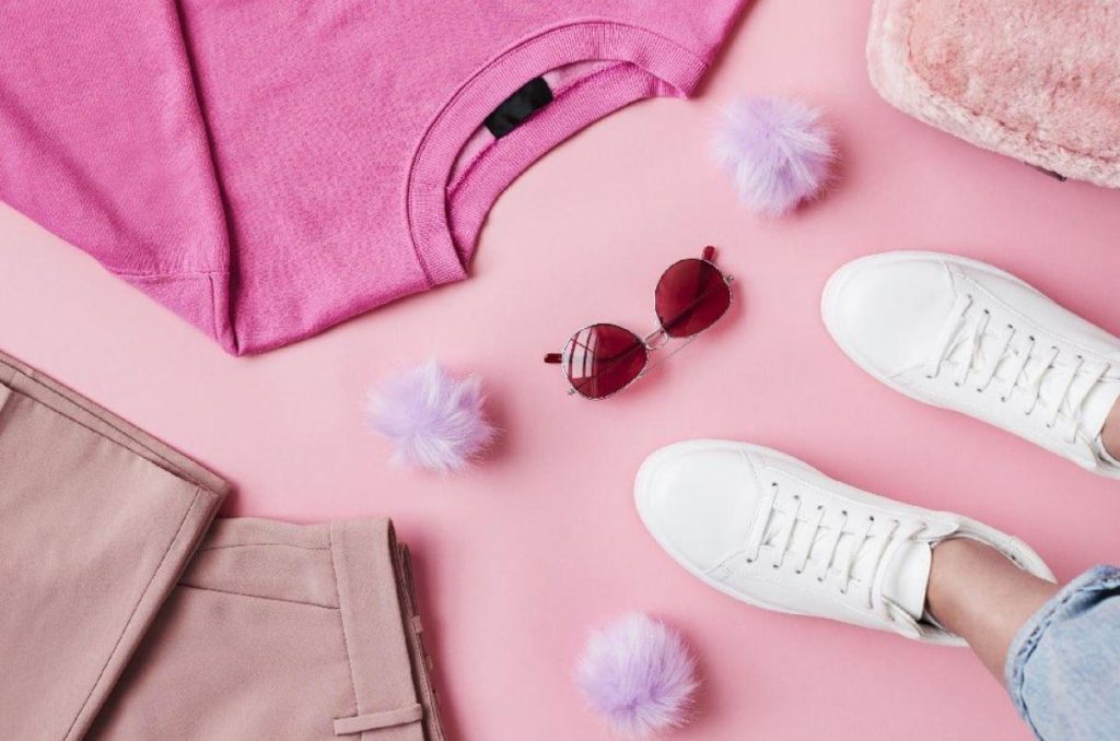 Prendas rosas, tenis blancos y lentes rojos acomodados sobre un fondo rosa