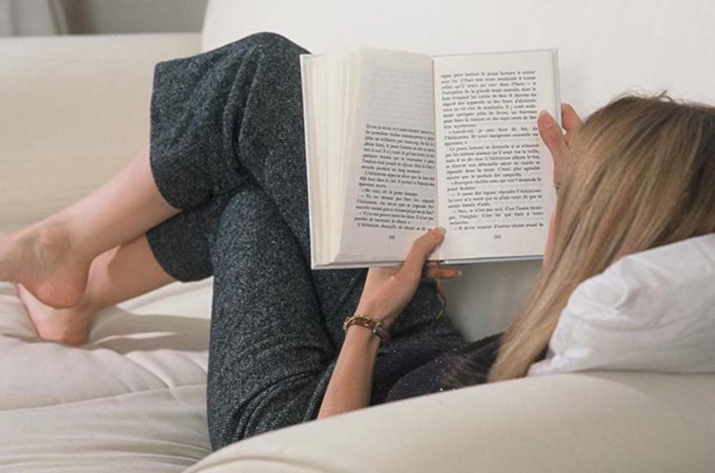 Mujer acostada en su sillón leyendo un libro, con las piernas cruzadas y cómoda postura de lectura