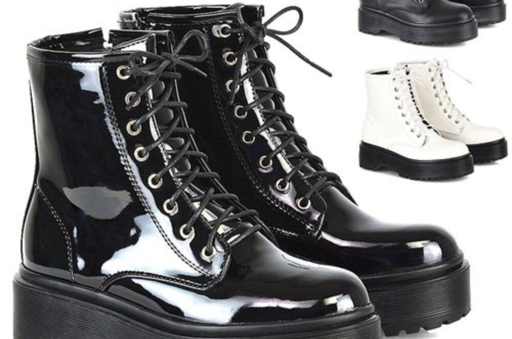 Botas negras de charol junto a unas botas blancas estilo punk rock sobre un fondo blanco