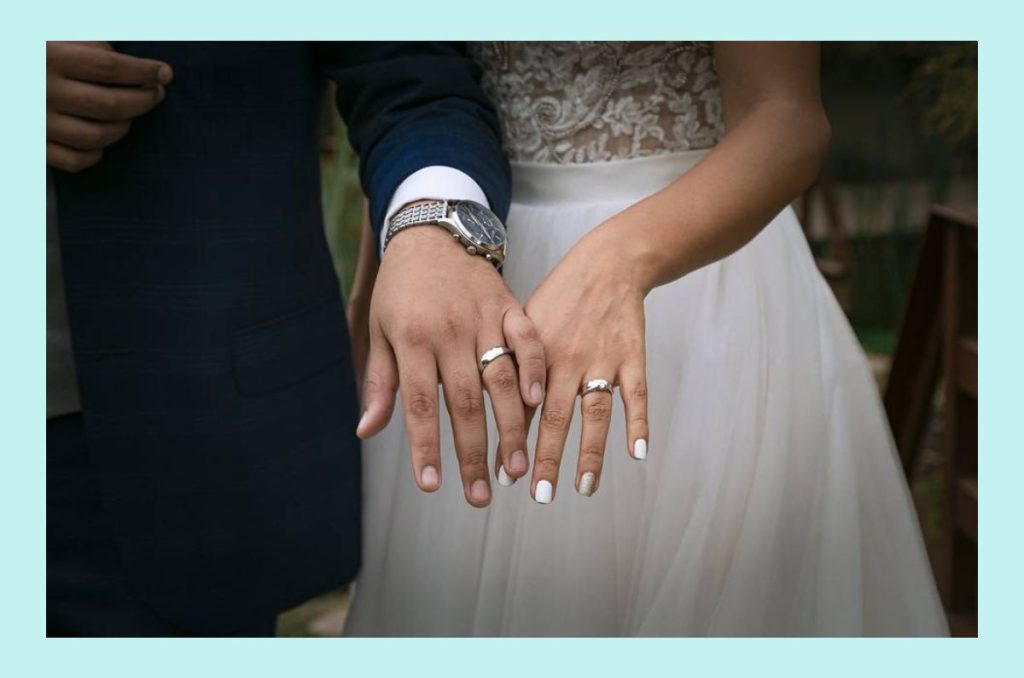 Pareja de recién casados tomados de la mano mostrando sus anillos de boda