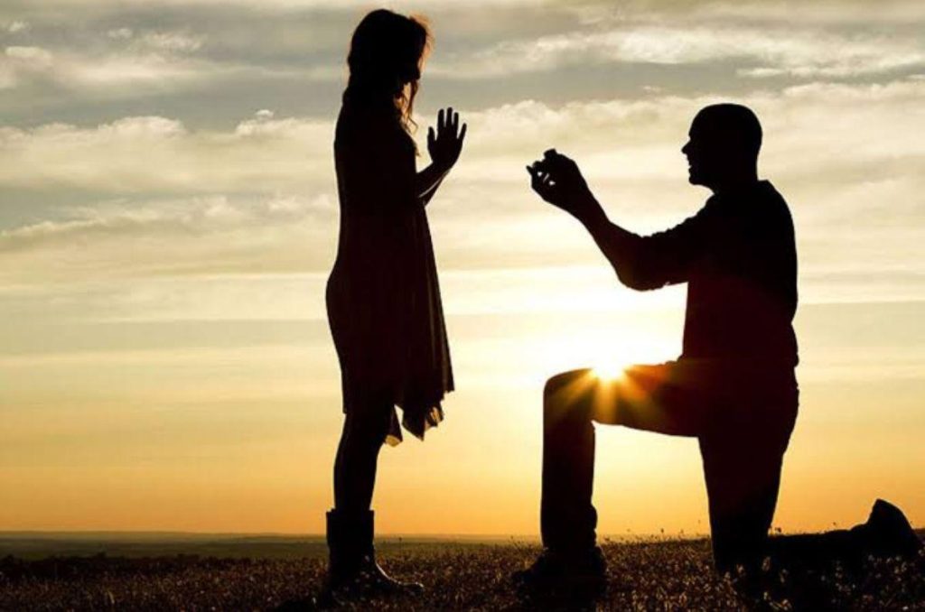 Sombras de una pareja durante una propuesta de matrimonio al atardecer, con el hombre hincado frente a la mujer