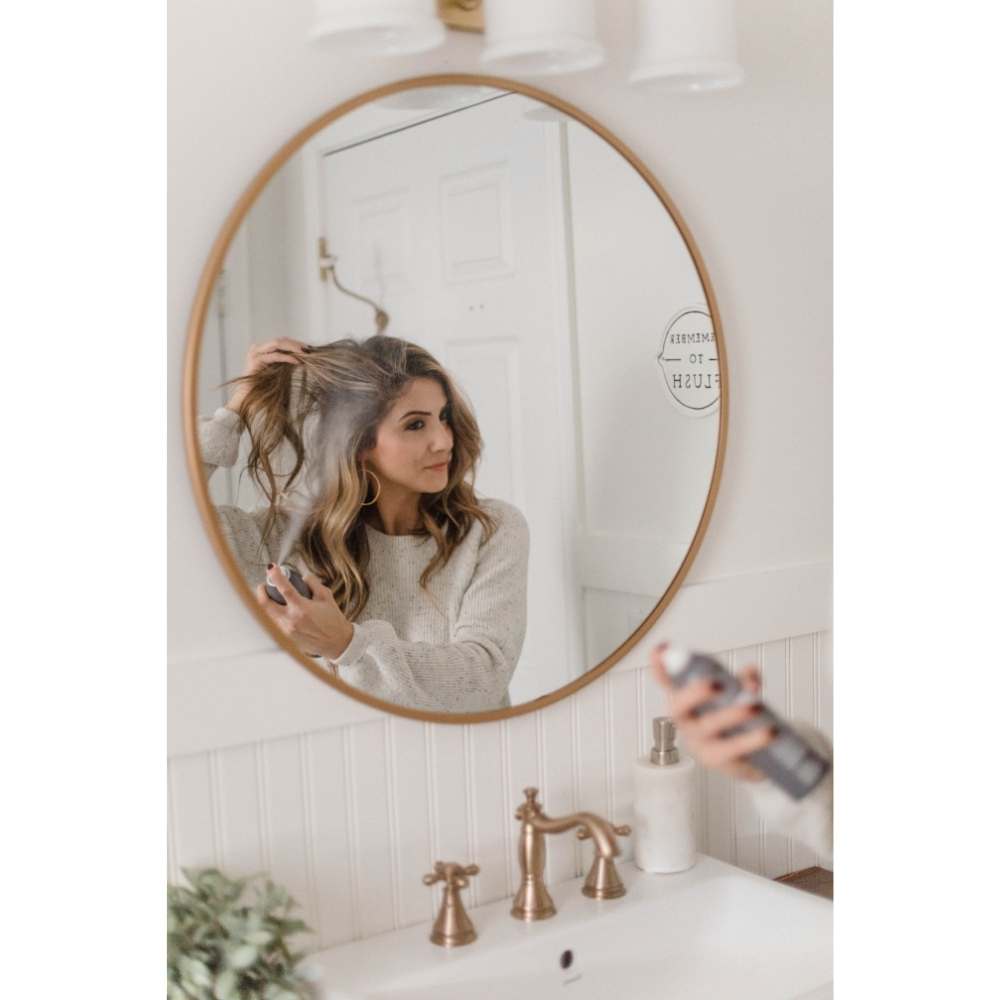 Chica frente al espejo rociando shampoo en seco en su cabello rubio