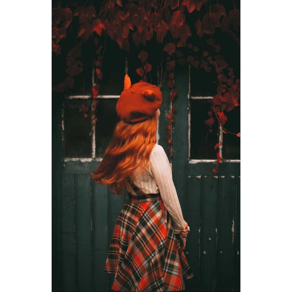 Chica con cabello largo cobrizo suelto arreglado con na boina estilo francés color roja