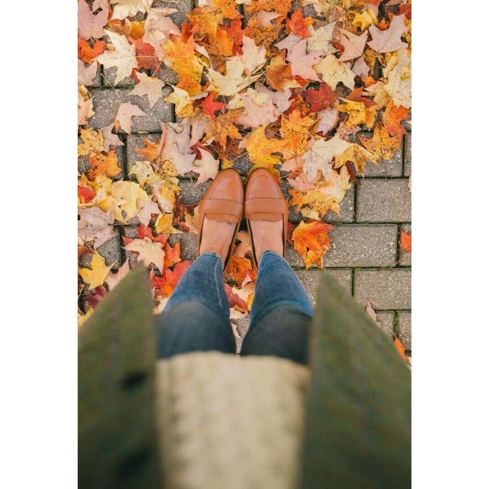 Fotografía en ángulo de picada de los pies y zapatos de una chica con hojas de otoño