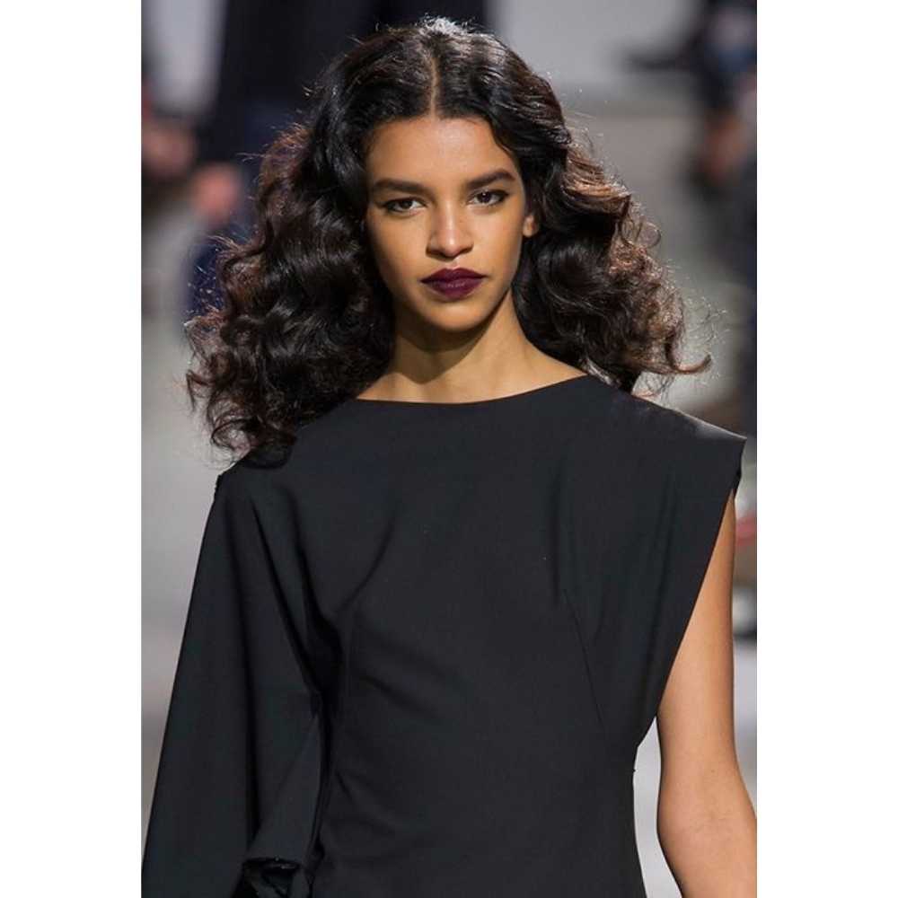 Modelo de piel morena en un atuendo negro con el cabello suelto y ondulado luciendo labios vino oscuro