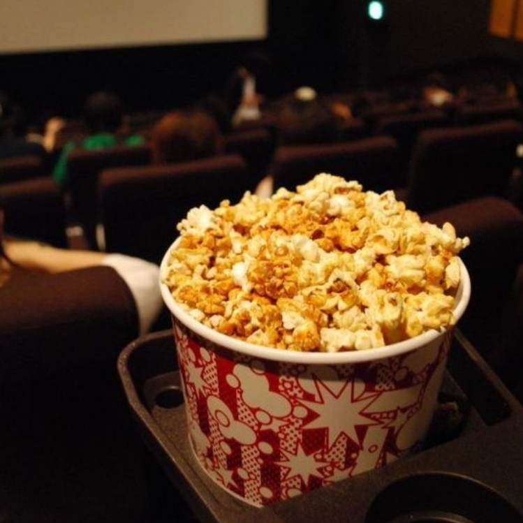 Fotografía dentro de una sala de cine enfocando a una cubeta de palomitas de mantequilla