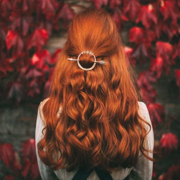 Chica de espaldas en un bosque d ehojas rojas de fondo con cabello largo semi suelto color cobrizo y ondulado