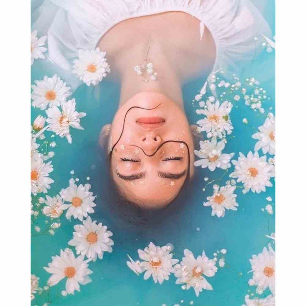 Chica en bañera recostada con agua y flores para ritual con sal