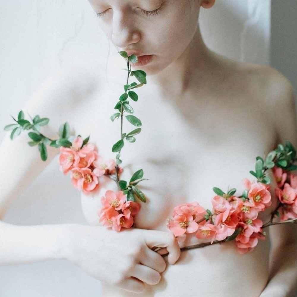 Mujer pálida desnuda de la parte superior con ramilletes de flores subriendo sus pechos