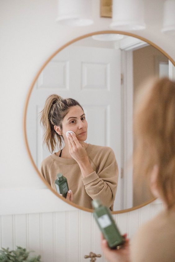 Mujer viendose al espejo para limpiarse la cara