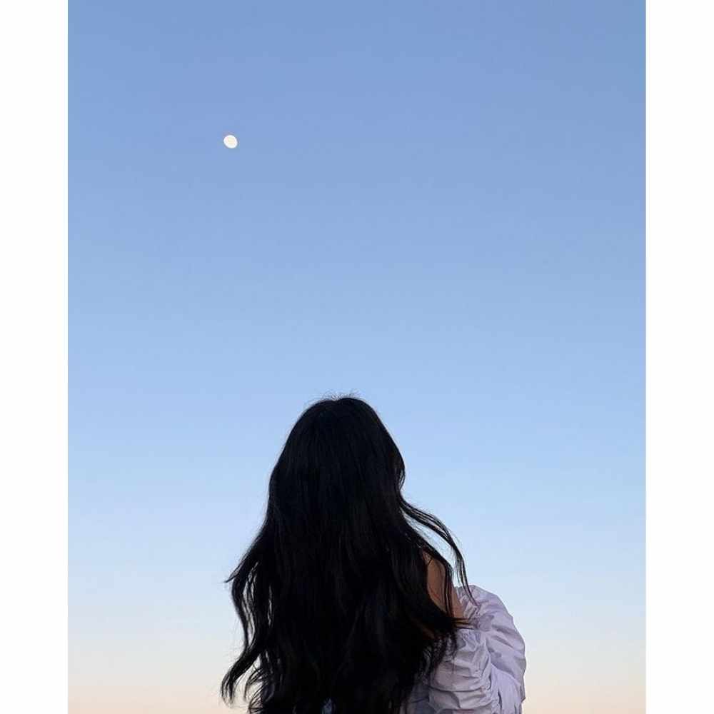 Chica bajo la luna llena con su cabello largo ondulado viendo la luna