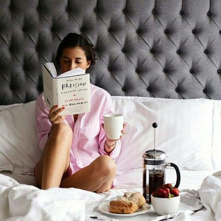 Chica leyendo en su cama y desayunando