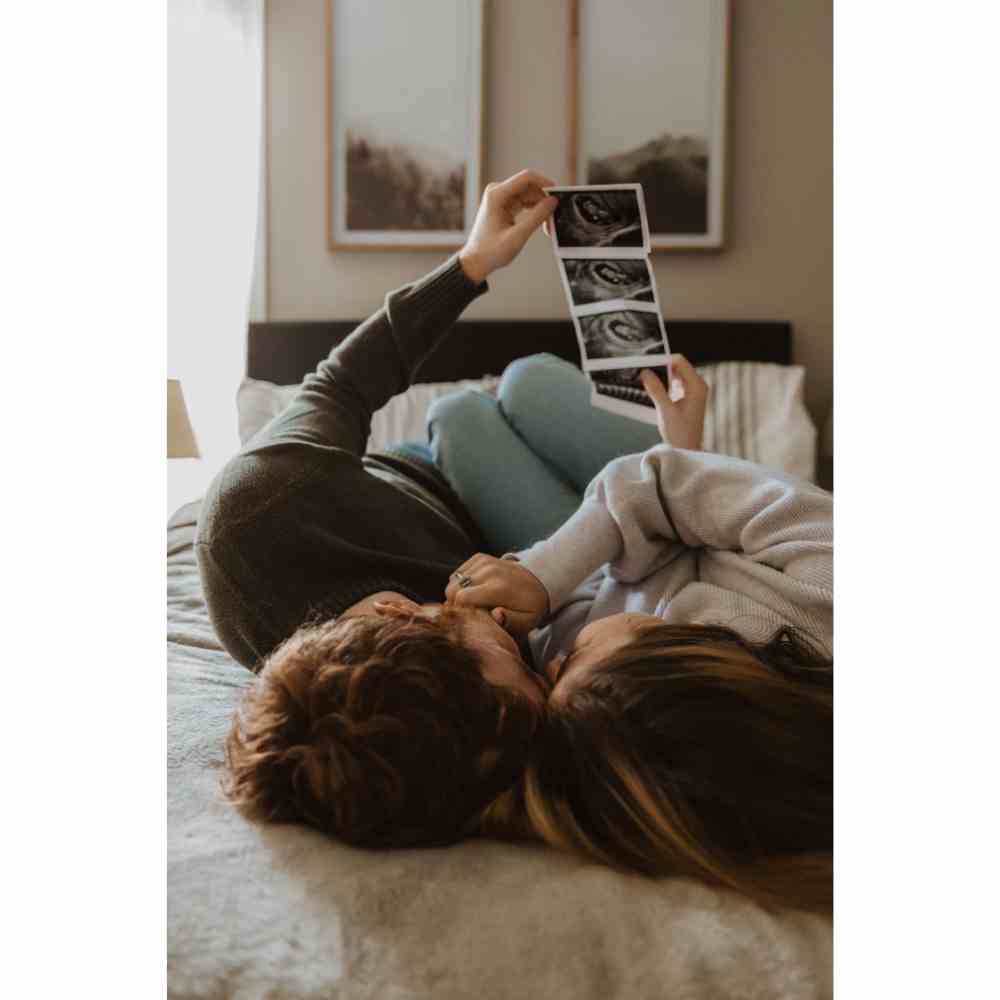 Pareja recostada en su cama viendo fotos de ultrasonido