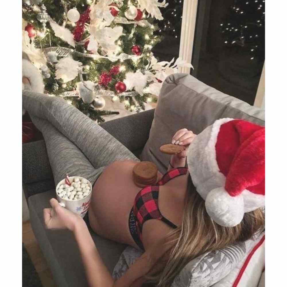 Chica embarazada cenando galletas frente a árbol de navidad