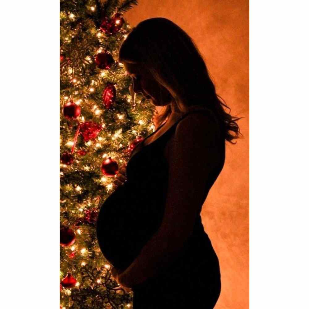 Chica embarazada en pose navideña frente a su árbol de Navidad