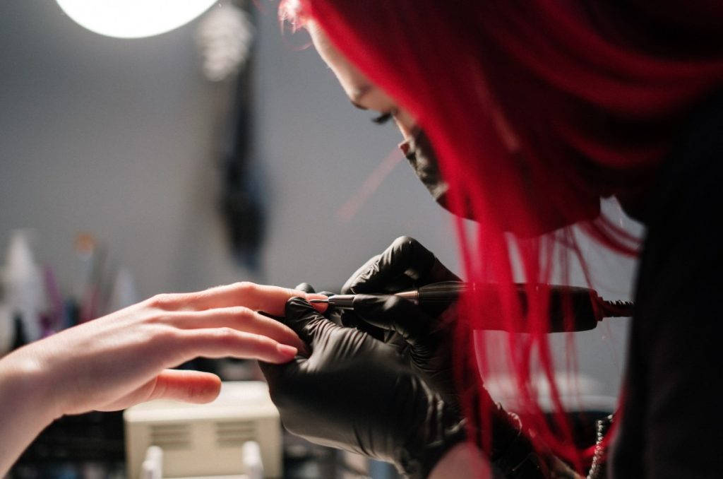 manicurista profesional con guantes y cubrebocas, lampara para uñas