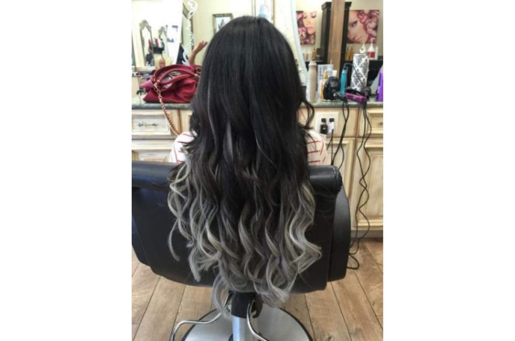 Mujer de espaldas mostrando su cabello largo, negro y ondulado con puntas platinadas que iluminan el look y ayudan a disimular las canas