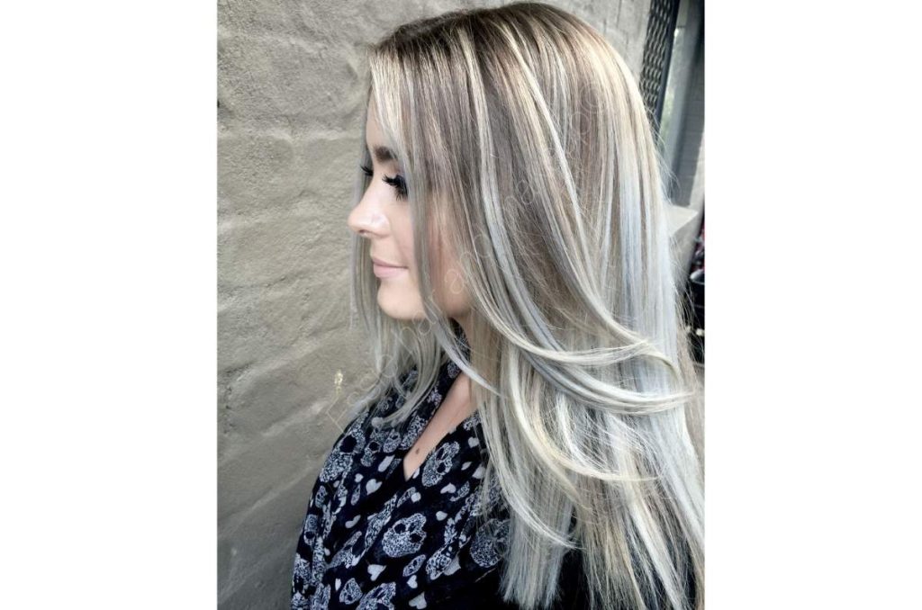 Mujer de lado mostrando su cabello negro con mechones platinados en técnica balayage en capas, logrando dimensión y disimulando las canas con naturalidad