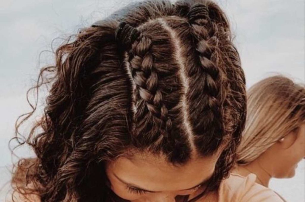 Chica con cabello chino peinado con dos trenzas pegadas al cráneo en la parte superior y el resto del cabello suelto, un look moderno y divertido, ideal para peinados fáciles y girly para cabello chino