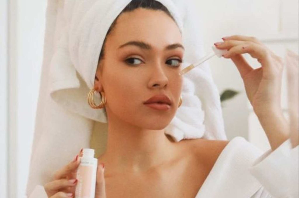 Mujer con bata y toalla en la cabeza aplicándose un sérum facial.