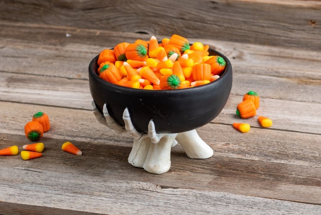 Recipientes decorados con motivos de Halloween como calabazas, fantasmas y calaveras, llenos de dulces.