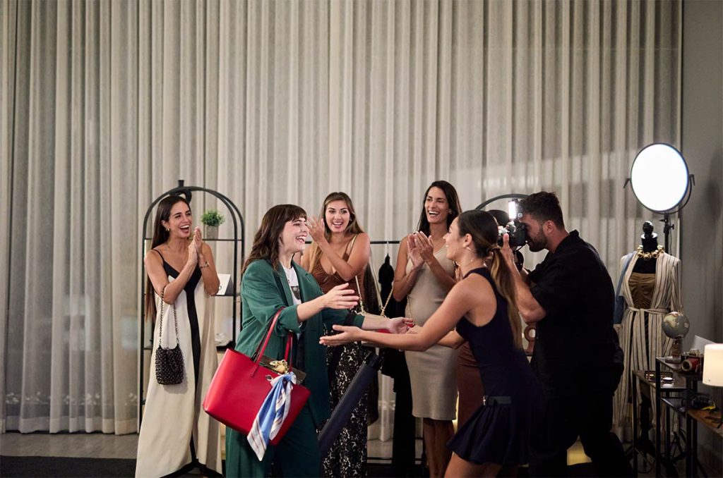 Mujeres en un cuarto en un hotel de lujo con un camarógrafo tomándoles fotos llamativas con cortinas blancas de fondo