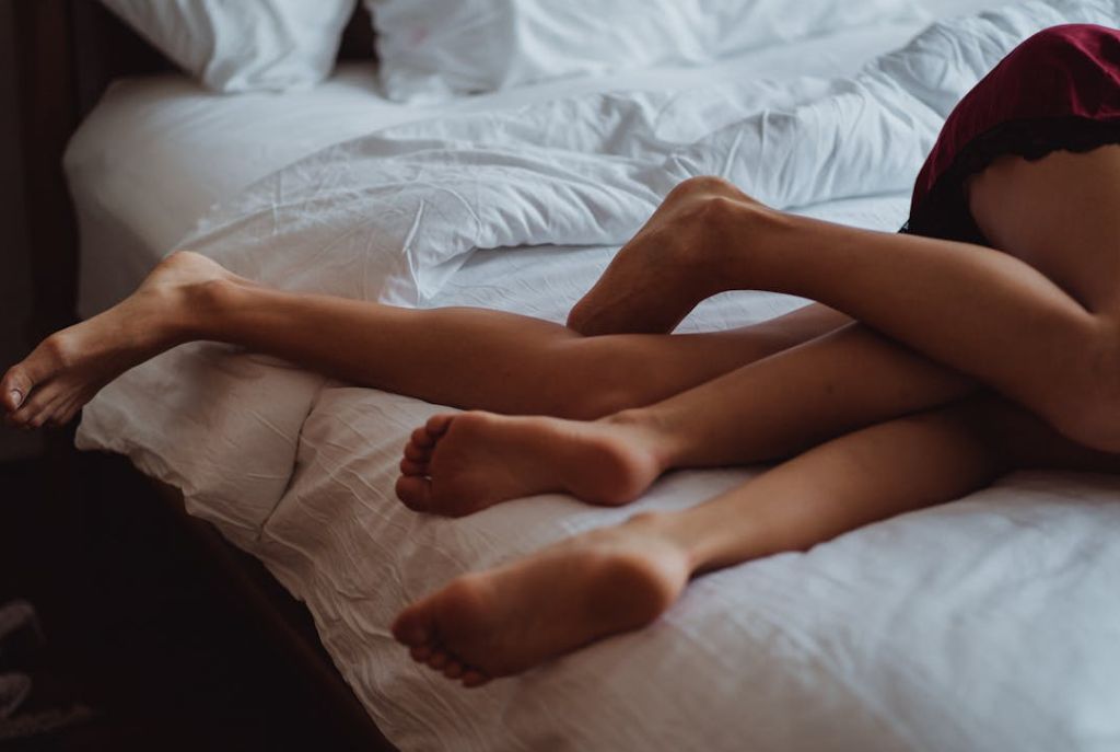 Piernas de pareja acostadas juntas al borde de la cama en una habitación de motel, mostrando cercanía y complicidad