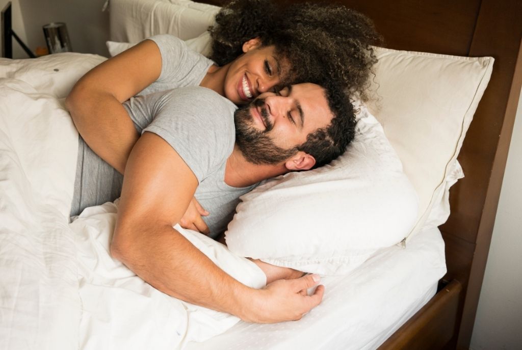 Pareja abrazada en la cama despertando con una sonrisa, compartiendo cercanía y complicidad