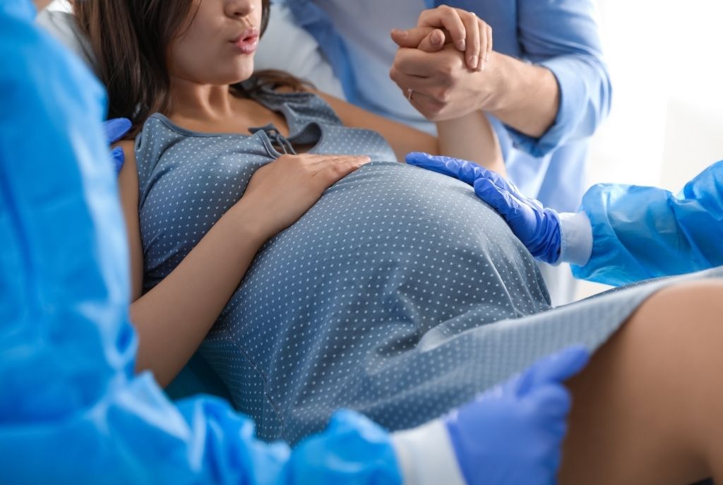 Una mujer embarazada a punto de dar a luz en el hospital, su esposo la acompaña y le sostiene la mano mientras ella hace ejercicios de respiración, una forma natural de cómo llegan los bebés al mundo