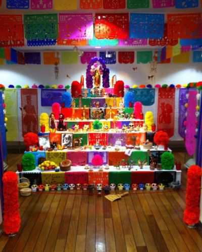 Ofrenda colorida de Día de Muertos: comoda, papel picado, velas y fotografías