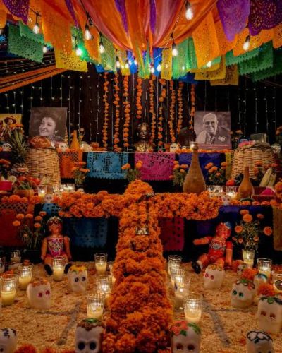 Altar de muertos con platillos tradicionales y decorada con flores de cempasúchil y papel picado