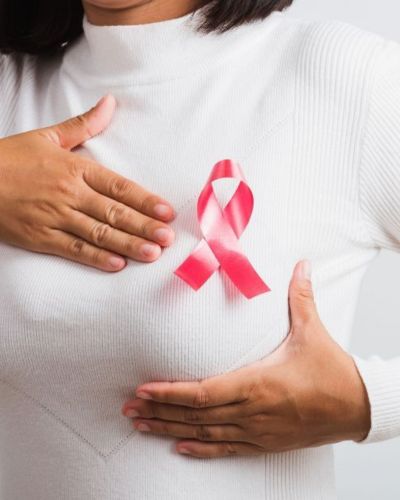 Mujer vistiendo blusa blanca de cuello sosteniendo un lazo rosado cerca del pecho