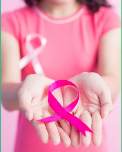 Mujer usando blusa color rosa sosteniendo el moño rosa, símbolo del cáncer de mama