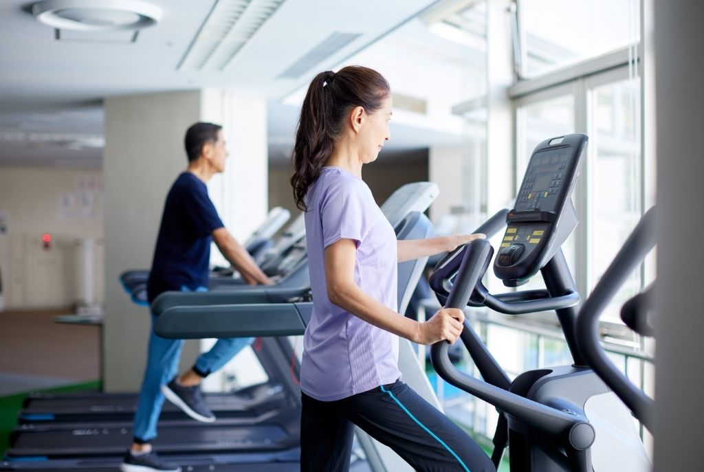 Mujer haciendo ejercicio en la caminadora del gimnasio, vistiendo ropa deportiva, con postura activa y concentrada