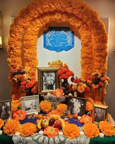 Altar de muertos con fotografías y arco de flor de cempasúchil