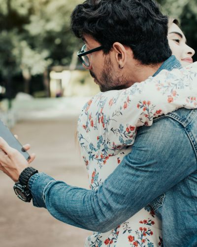 Hombre abraza a su pareja mientras revisa su celular de espaldas