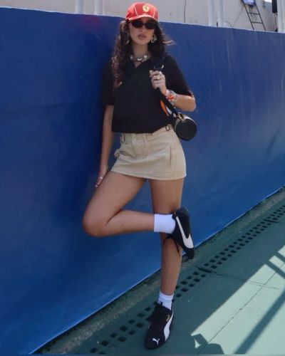 Outfit con shorts beige, camisa polo oscura, tenis negros, calcetas largas y gorra de la Fórmula 1