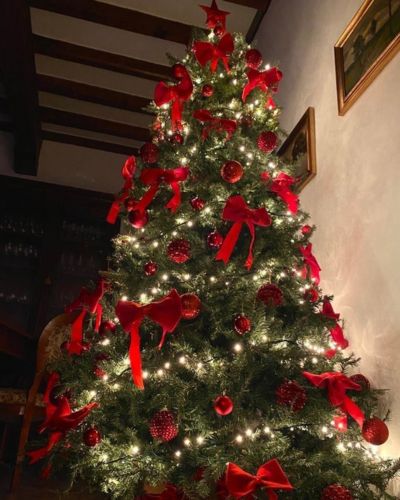 Árbol decorado con moños terciopelo, esferas color rojo y luces amarillas