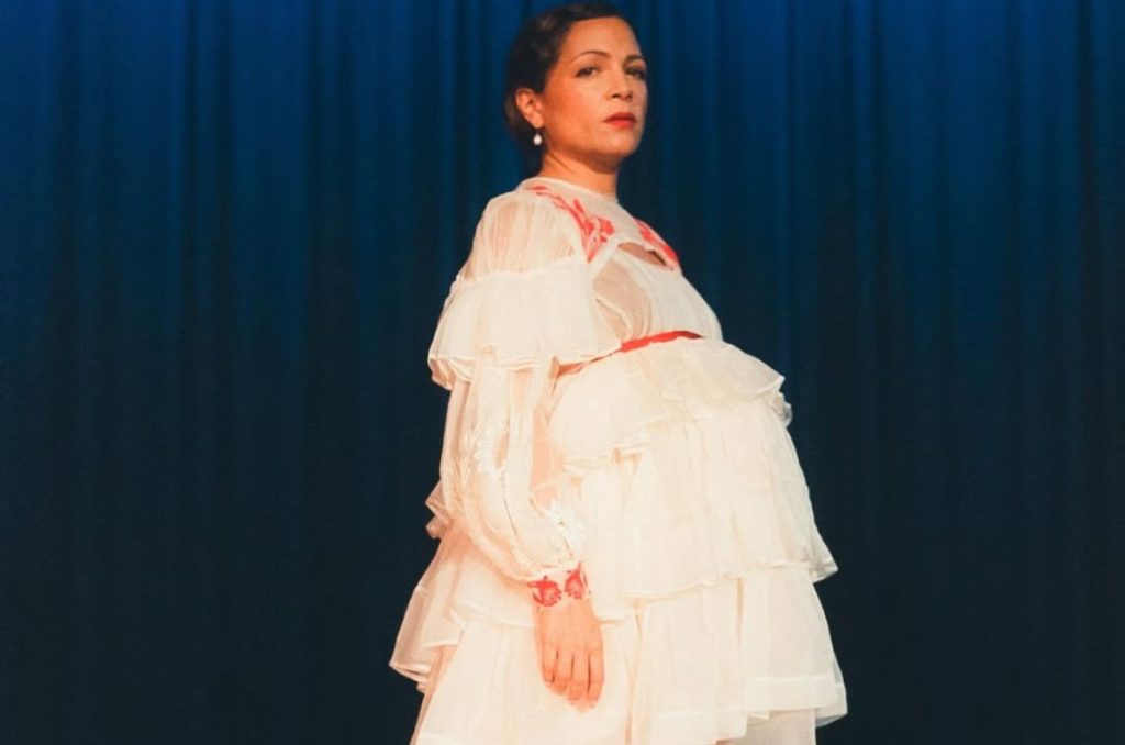Intérprete de "Hasta la raíz" embarazada, usando un vestido con holanes en color blanco