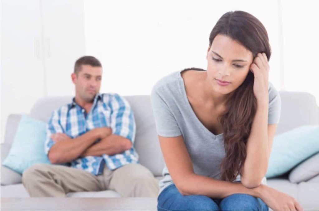 Pareja con ánimo bajo después de una discusión; él sentado al fondo con los brazos cruzados y ella al frente en pose pensativa, peleas más comunes en el primer año de matrimonio