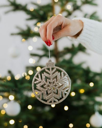 Mujer con decoración navideña en la mano cerca del árbol de navidad