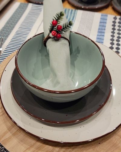 Montaje de mesa navideña en Casaideas: plato, bowl verde menta y servilleta con aro de pino y bayas rojas sobre base de madera.