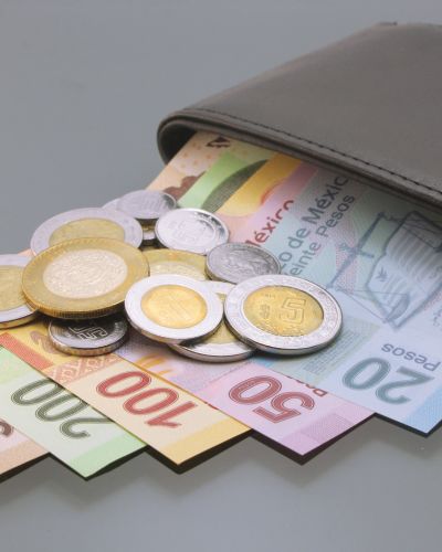 Billetes mexicanos de 100, 200, 500 y 1000 pesos asomándose de una cartera negra sobre una superficie de madera.