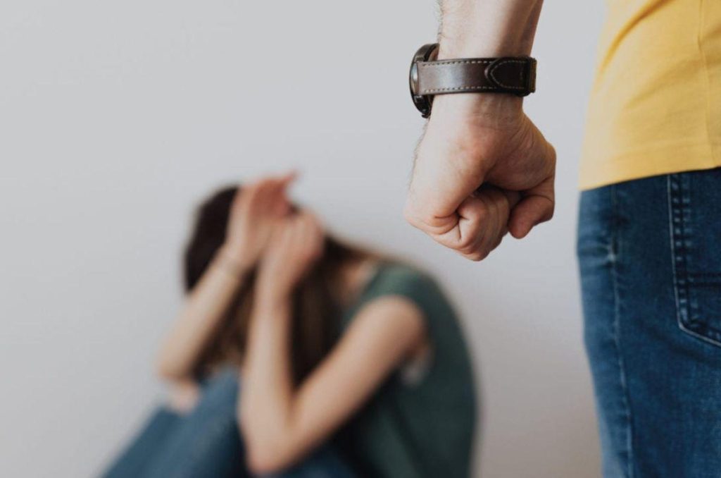 Mujer sentada en el piso cubriéndose con miedo ante la presencia amenazante de un hombre