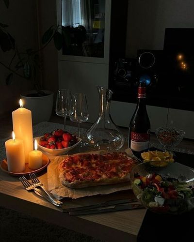 Foto en plano general de cocina bajo la luz de las velas con una pizza casera como cena romántica del Día de San Valentín