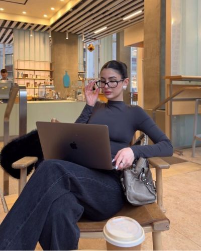 Foto de mujer sentada con una computadora en las pierdas, luciendo colores elegantes para el trabajo en un look de pantalones anchos y blusa de cuello alto en color gris piedra