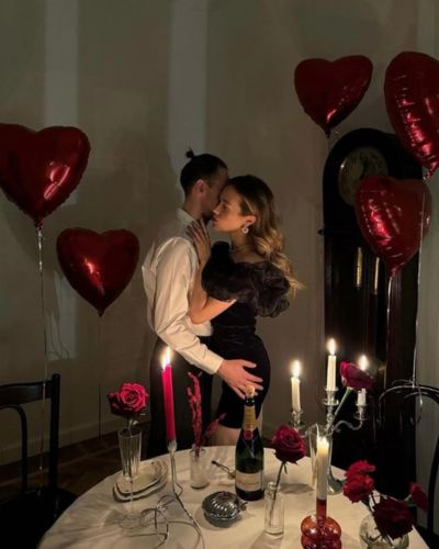 Foto de pareja celebrando el 14 de febrero con una cena romántica, la decoración es con velas, flores y globos en forma de corazón